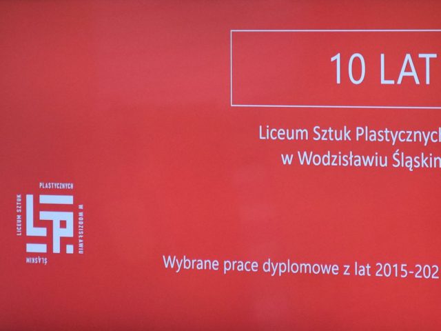 Widok na tytuł wystawy. 10 lat Liceum Sztuk Plastycznych w Wodzisławiu Śl. Wybrane prace dyplomowe z lat 2015-2021. Białe napisy na czerwonym tle