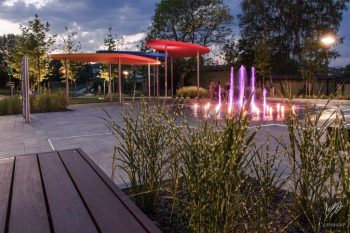 park sensoryczny, na zdjęciu wybetonowany plac, podświetlana fontanna oraz donice z roślinami