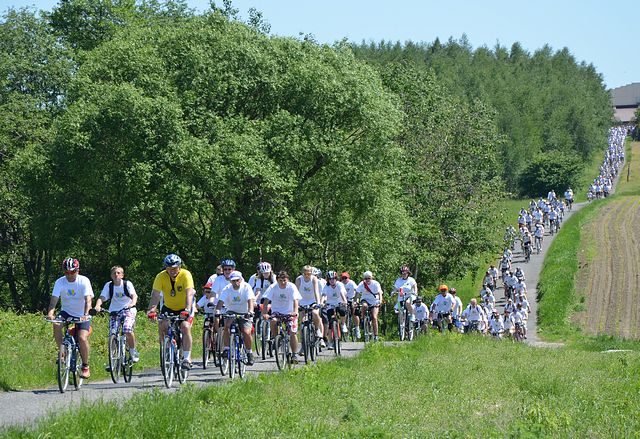 Uczestnicy powiatowego rajdu rowerowego jadący peletonem; na zdjęciu kilkuset rowerzystów w białych koszulkach jadący malowniczą