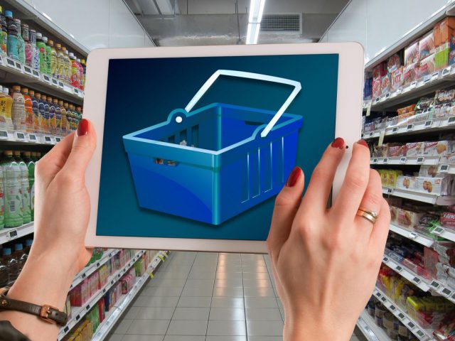 grafika przedstawiająca kobiecie dłonie, które trzymają koszyk na zakupy. W tle półki sklepowe z towarem spożywczym.