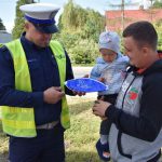 akcja Road Safety Days w Wodzisławiu Śl. 21 wrzesnia 2021, na zdjęciu kierowca trzymający na rękach dziecko, a policjant wręcza dziecku gadżet w postaci dmuchanej piłki