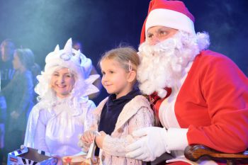 Na zdjęciu mężczyzna przebrany za Świętego Mikołaja, kobieta przebrana w biały strój oraz mała dziewczynka pozująca do zdjęcia
