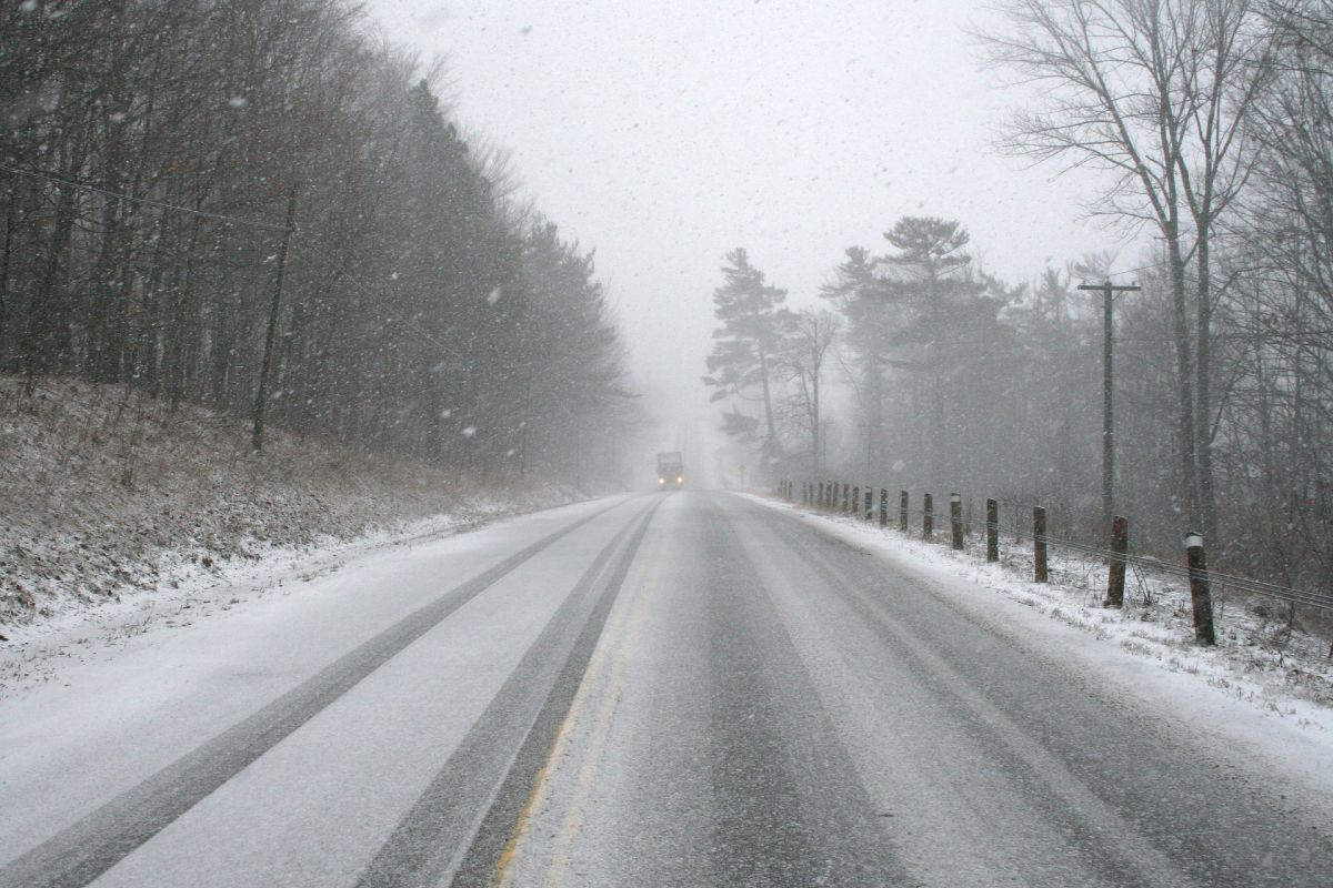 widok zaśnieżonej drogi, w tle ledwo widoczny wskutek opadów samochód ciężarowy
