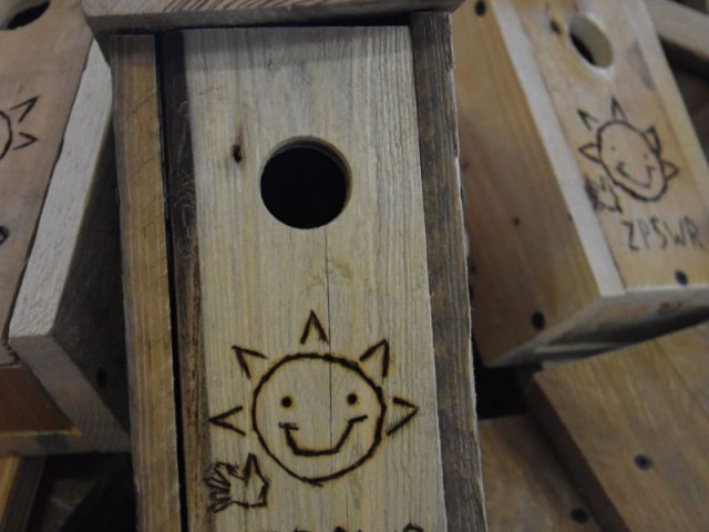 Drewniana budka lęgowa z wypalonym logo ZPSWR w kształcie uśmiechniętego słonka