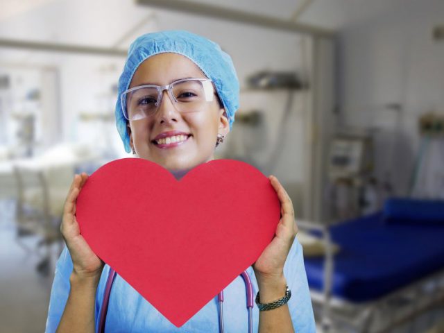 Kobieta w stroju medycznym trzymająca w dłoniach wielkie czerwone serce