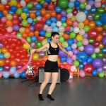 Uczennica dająca pokaz gimnastyki artystycznej w tle ściana z kolorowych balonów