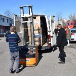 Cztery osoby, jedna z wózkiem widłowym pakują palety z kartonami na samochód dostawczy