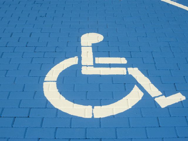 oznaczenie miejsca parkinngowego dla osoby z niepełnosprawnością, logo osoby na wózku na niebieskim tle