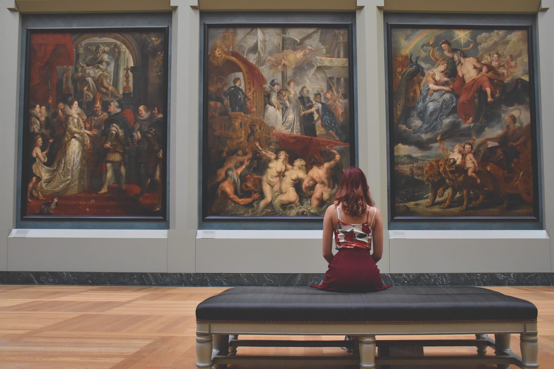 Kobieta sieząca na ławce, przed nią 3 obrazy w muzeum