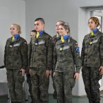 Uczniowie stoją w wojskowych mundurach i żółto-niebieskich chustach na szyi