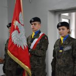 Uczniowie w mundurach wojskowych trzymają sztandar RP.