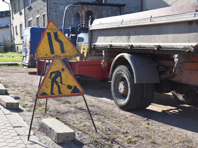 Znak drogowy informujący o robotach drogowych i zwężeniu jezdni. Za znakiem samochód ciężarowy.