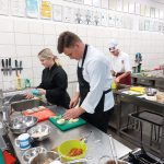 Uczniowie w fartuchach kucharskich szykują jedzenie w pracowni gastronomicznej.