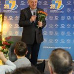 Paweł Porwoł przemawia do mikrofonu, w ręce trzyma bukiet tulipanów.