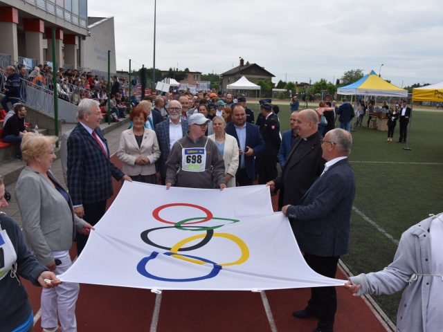 Osoby trzymające flagę olimpijską (białą flagę z 5 różnokolorowymi, przecinającymi się okręgami)