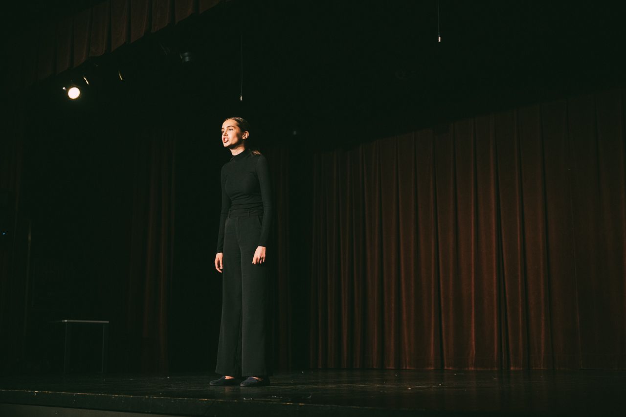 Ubrana na czarno Antonina Swoboda występuje na scenie, na scenie panuje półmrok.