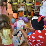 Dzieci rozpakowują prezenty. Na podłodze kolorowe balony.