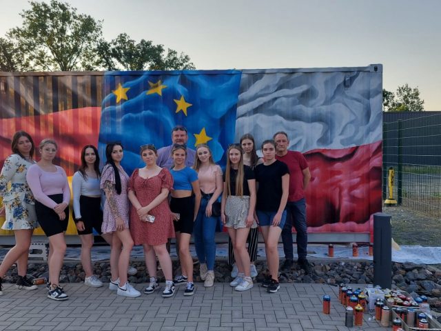 Zdjęcie grupowe młodzieży na tle graffiti w barwach narodowych Polski, Niemiec i UE