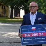 Leszek Bizoń trzyma w rękach bon. Na bonie kwota dofinansowania i flaga Polski.