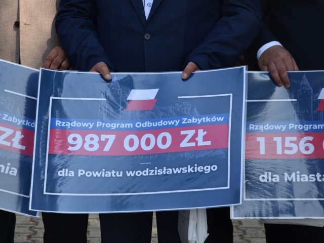 Zbliżenie na niebieski czek z flagą Polski i kwotą: 987 000 zł