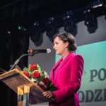 Uroczysta sesja Rady Powiatu Wodzisławskiego. Przy mównicy stoi senator i trzyma kwiaty.