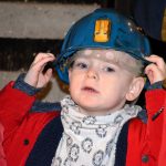 Kilkuletni chłopczyk w czerwonej kurtce i niebieskim kasku górniczym w sztolni.