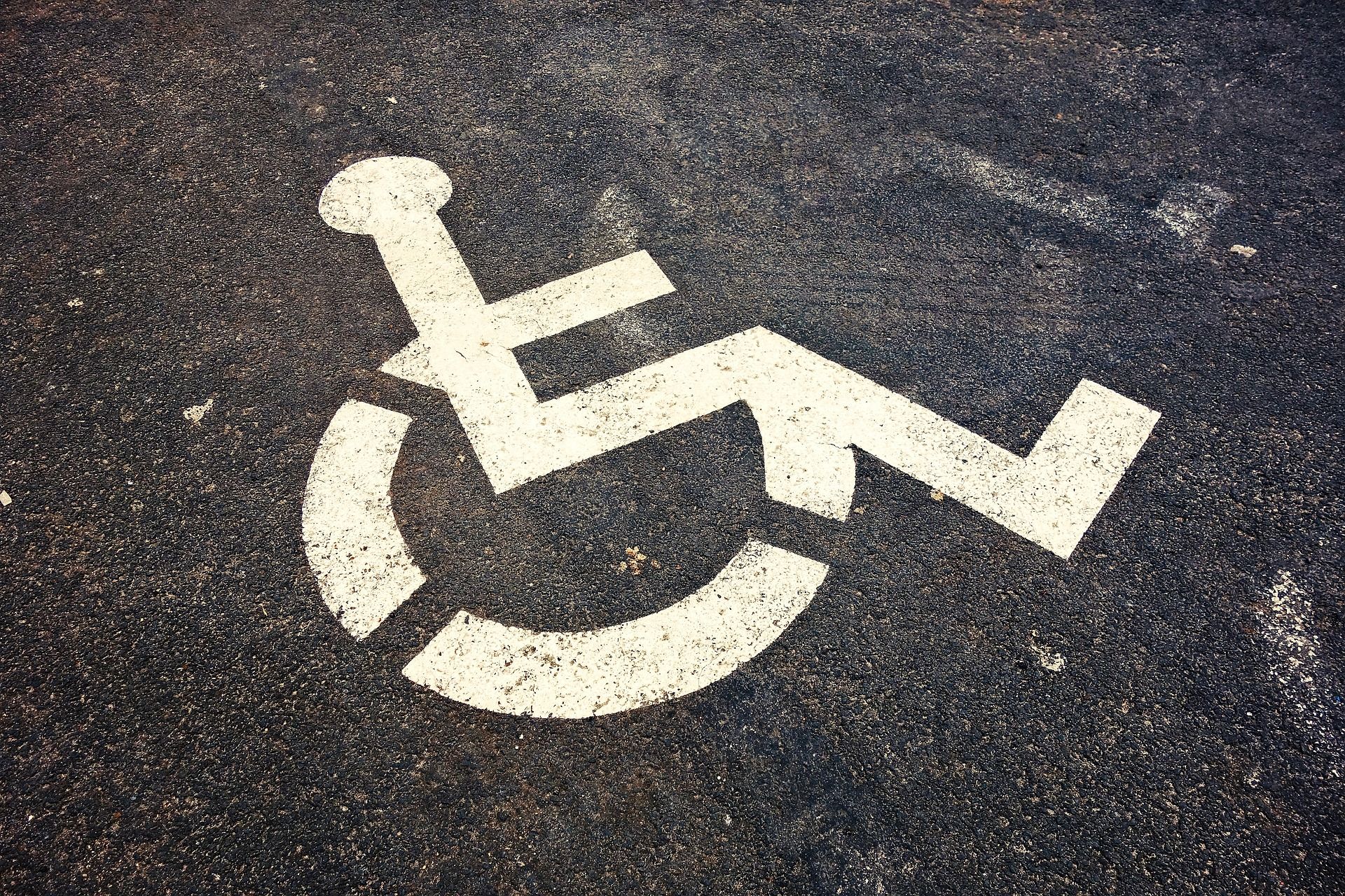 znak osoby na wózku inwalidzkim namalowany białą farbą na czarnym asfalcie