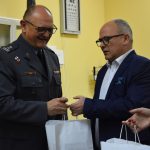 Leszek Bizoń wręcza torebkę prezentową pułkownikowi. Torebka jest biała z logo powiatu
