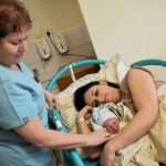 Kobieta tuli noworodka, obok stoi położna
