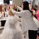 Uczennica układa fryzurę na kobiecie w sukni ślubnej