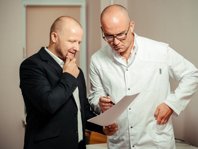 Dwóch mężczyzn, lekarz i pacjent, oglądający kartkę papieru