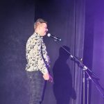 Chłopak stoi na scenie i śpiewa do mikrofonu
