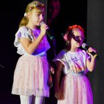 Dwie dziewczynki stoją obok siebie i trzymają w rękach mikrofony