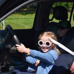 Dziewczynka w okularach siedzi za kierownicą samochodu.