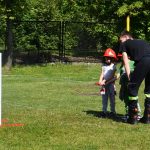 Dzieci testują sprzęt strażacki. Strażak stoi obok i pomaga