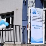 Baner z napisem Dzień Promocji Zdrowia przed drzwiami przychodni, z przodu białe i niebieskie balony