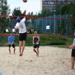 Zawodnicy w strojach sportowych grają w siatkówkę na piasku.