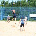 Zawodnicy w strojach sportowych grają w siatkówkę na piasku.