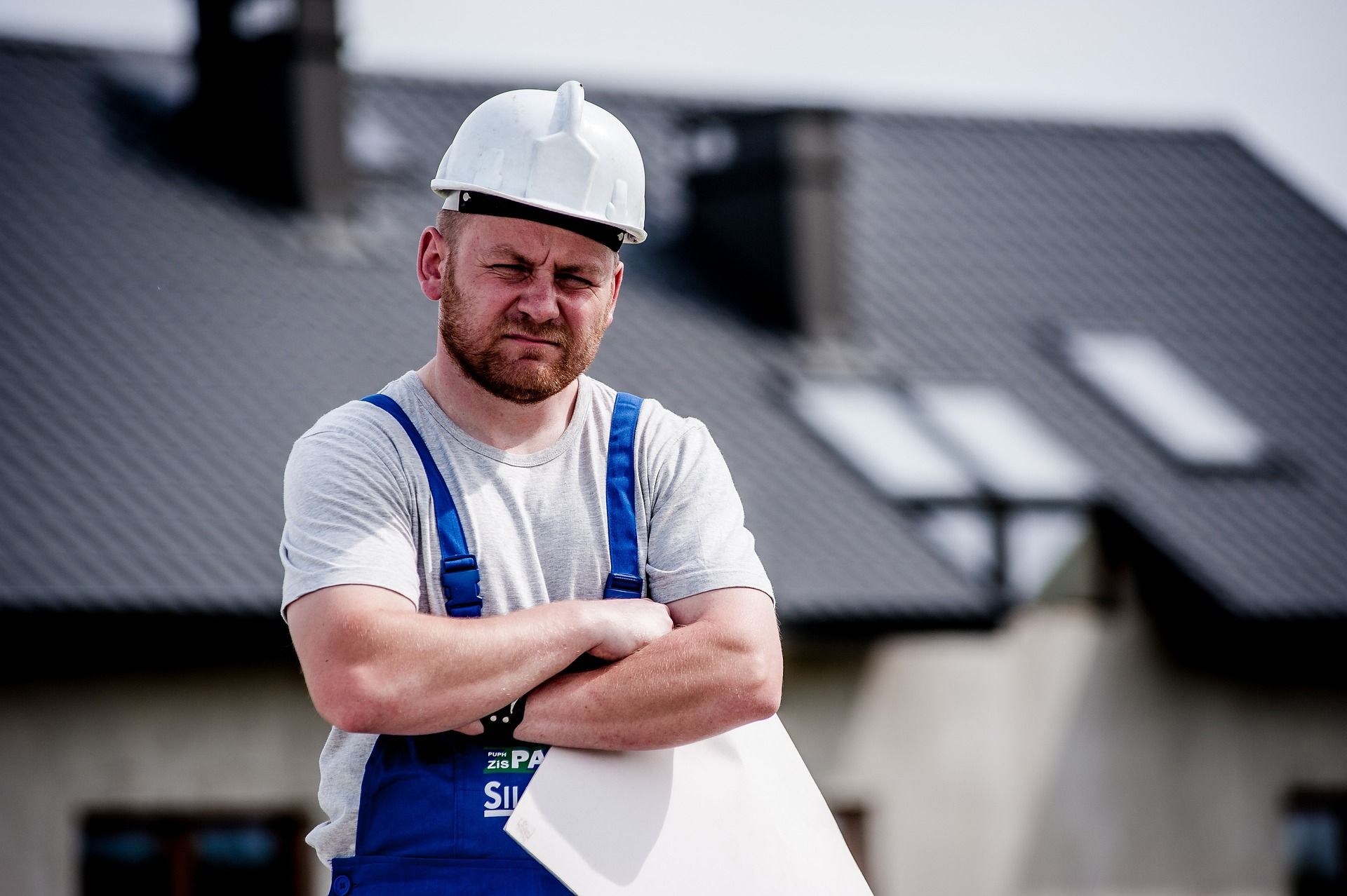 mężczyzna w kasku, trzymający w ręku projekt budowlany, w tle budynek w trakcie budowy