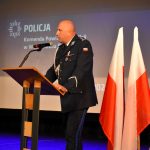 Przy mównicy stoi z-ca komendanta wojewódzkiej policji w Katowicach, Obok stoją trzy fagi biało-czerwone.